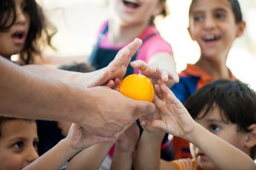 Niños tomando una naranja de la mano  de alguien